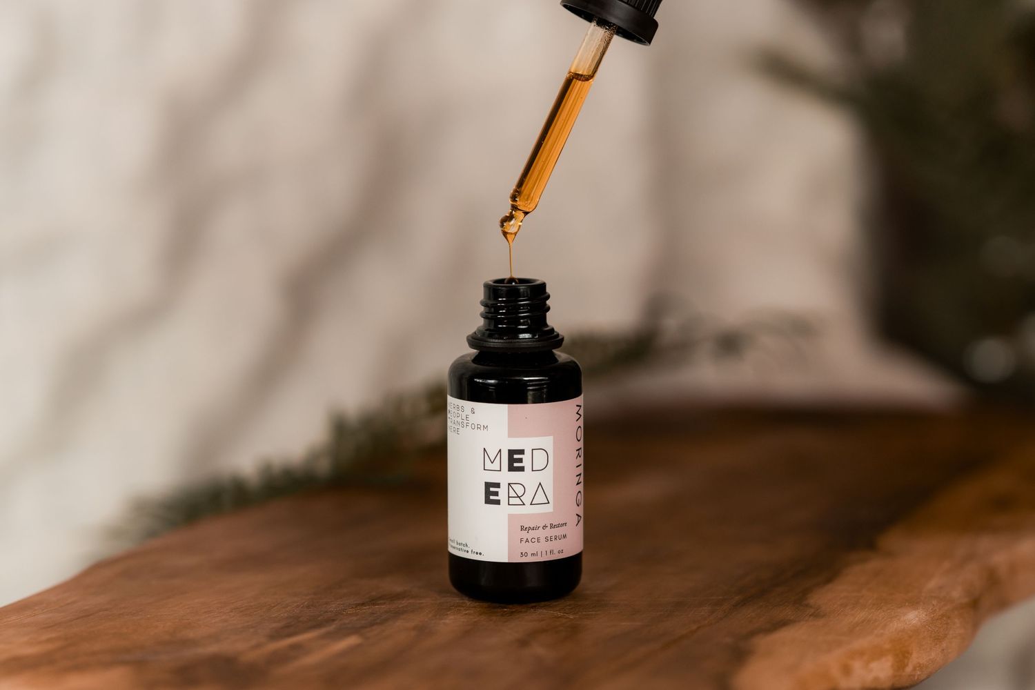 A dropper bottle with CBD oil being dispensed with an amber glass dropper over a wooden surface.