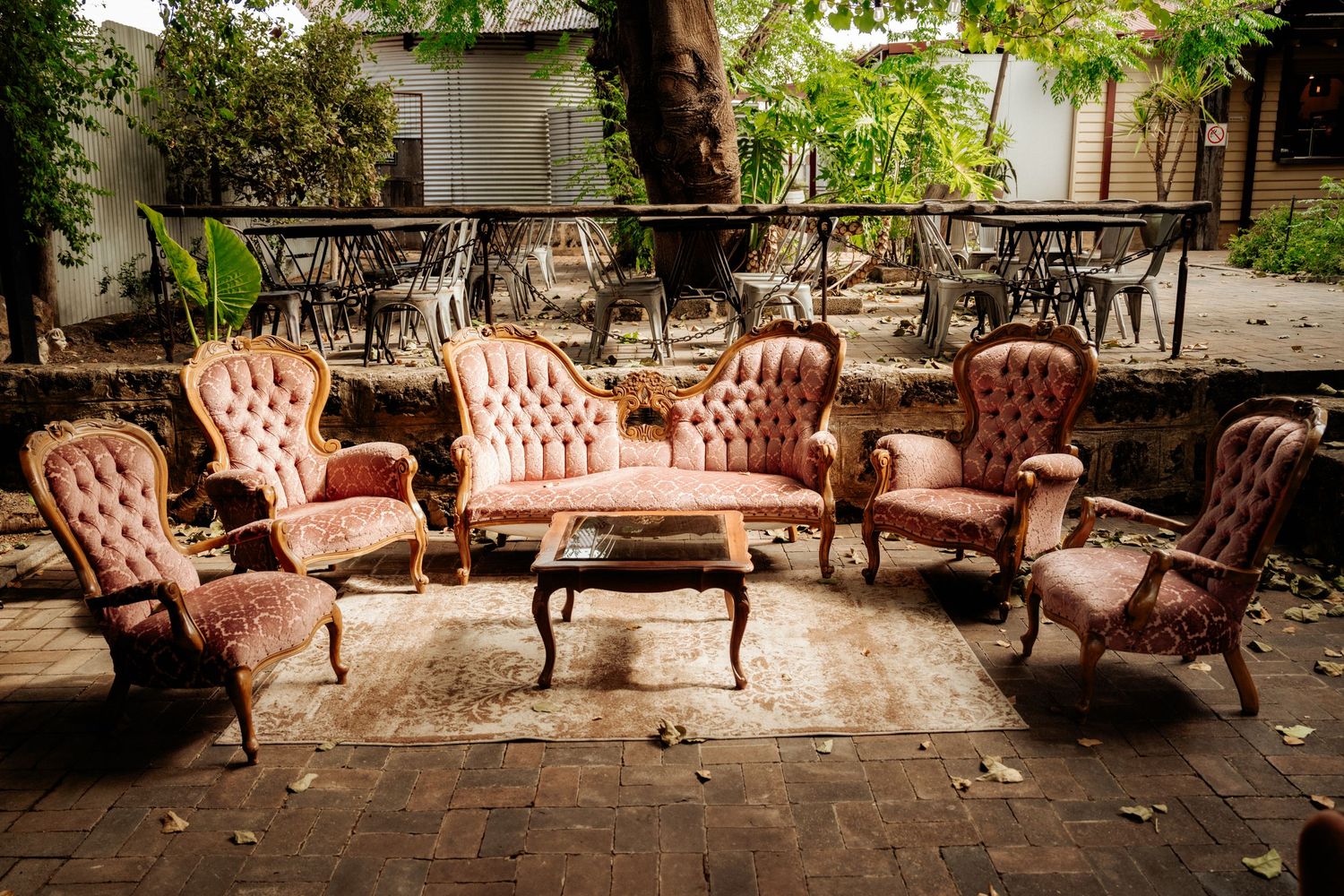 Elegant vintage pink velvet Victorian furniture set arranged on an outdoor brick patio with garden views.