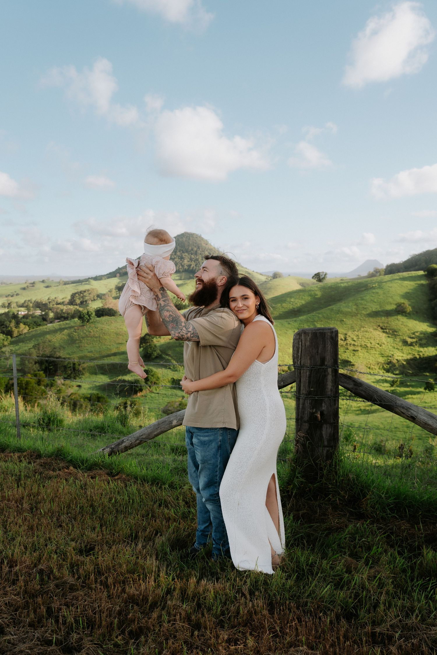 A family portrait set against lush rolling hills and blue sky.