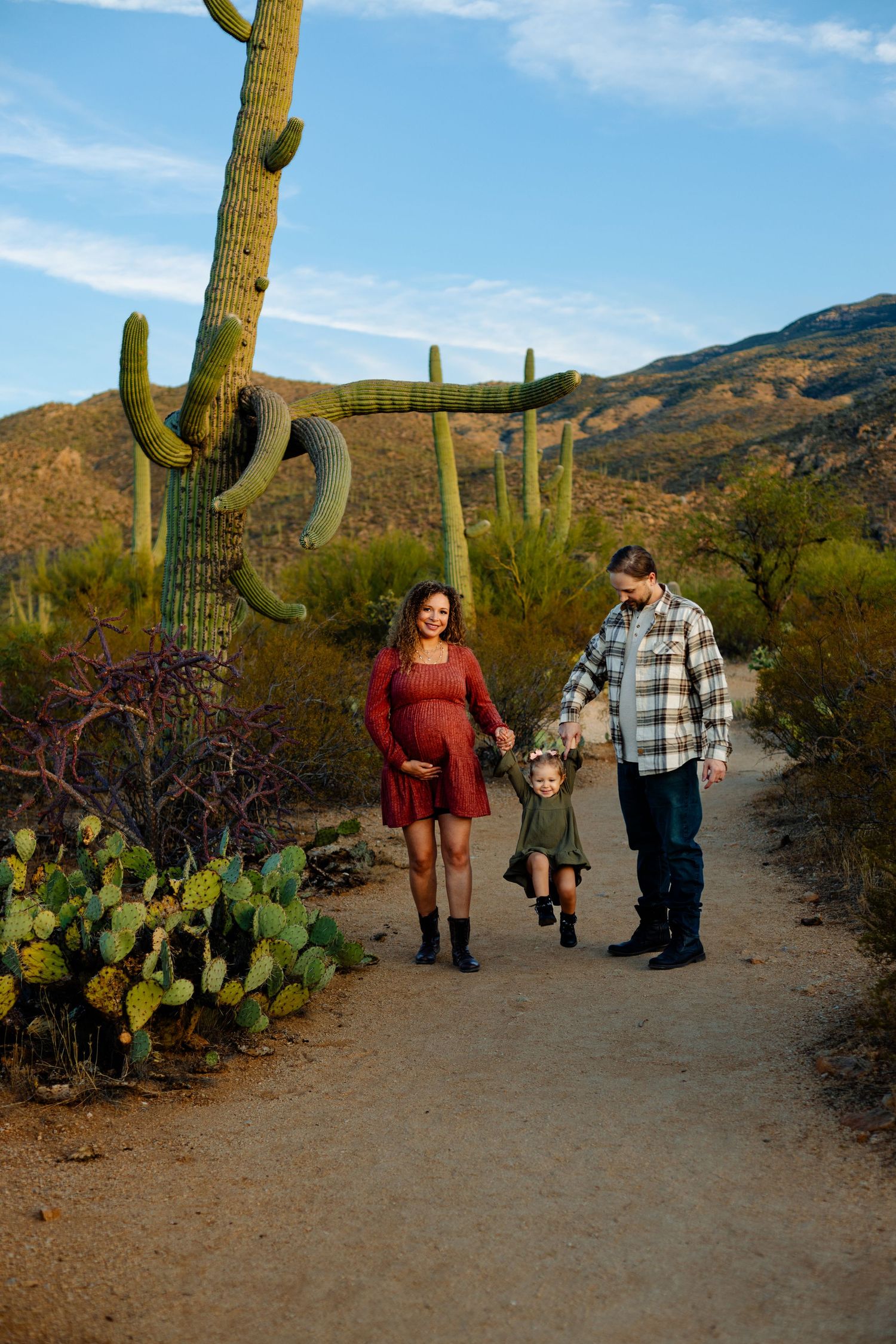 Family and expecting mother take a sunset walk along desert trail with towering saguaro cacti.