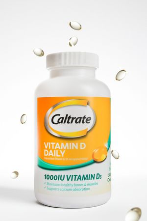 A bottle of Caltrate Vitamin D Daily supplement with 1000IU dosage and floating gel capsules against white background.