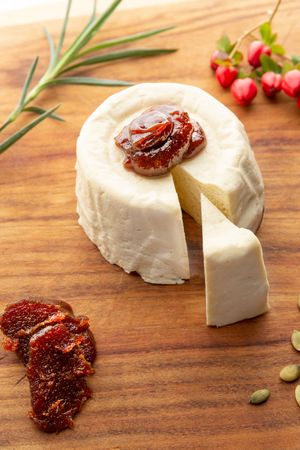 Fresh goat cheese wheel with sun-dried tomatoes and herbs served on wooden cutting board with rosemary garnish.