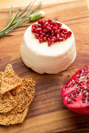 White creamy brie cheese wheel with pomegranate seeds and crispy crackers on a rustic wooden surface.