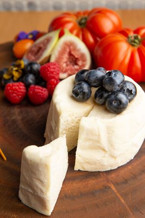 Fresh berries and tomatoes complement soft white goat cheese on a rustic wooden cutting board.