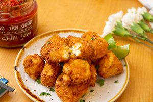 Golden fried chicken nuggets served on a white plate with garnish and chili jam jar in the background.