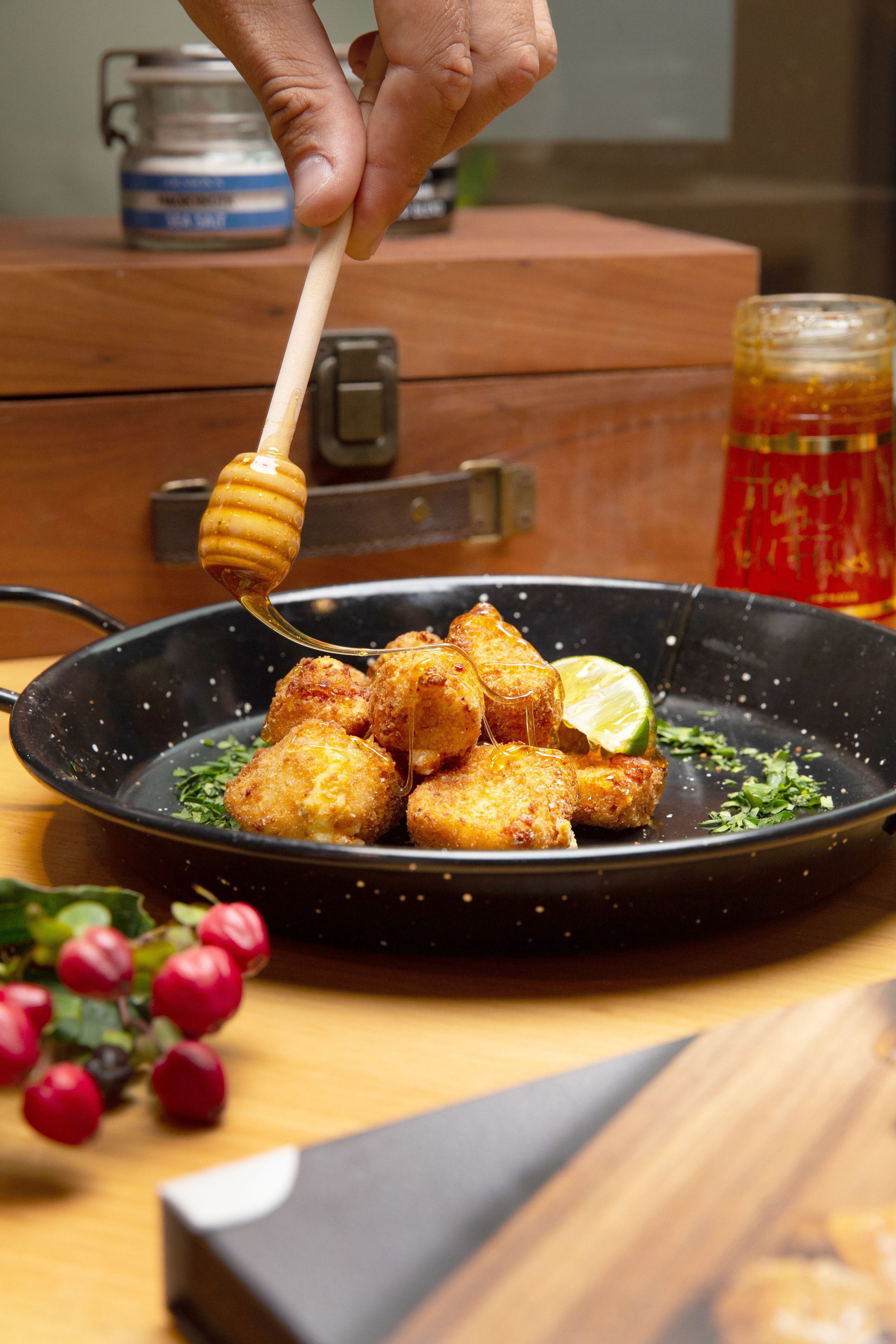 Honey drizzling over crispy pan-seared scallops with herbs and lemon in a black skillet, fresh radishes on wooden table.