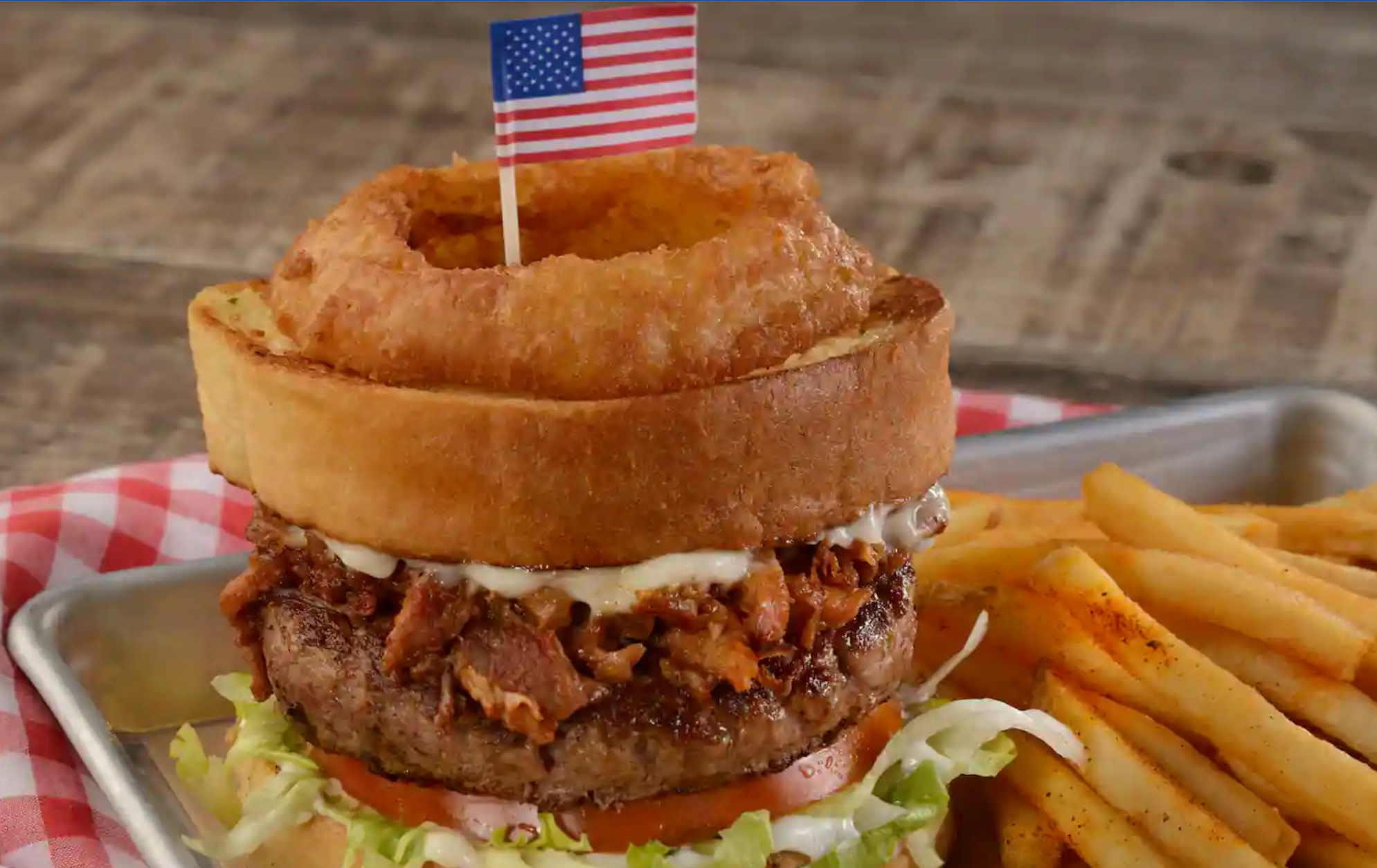 Gourmet burger with onion ring and American flag on brioche bun served with french fries.
