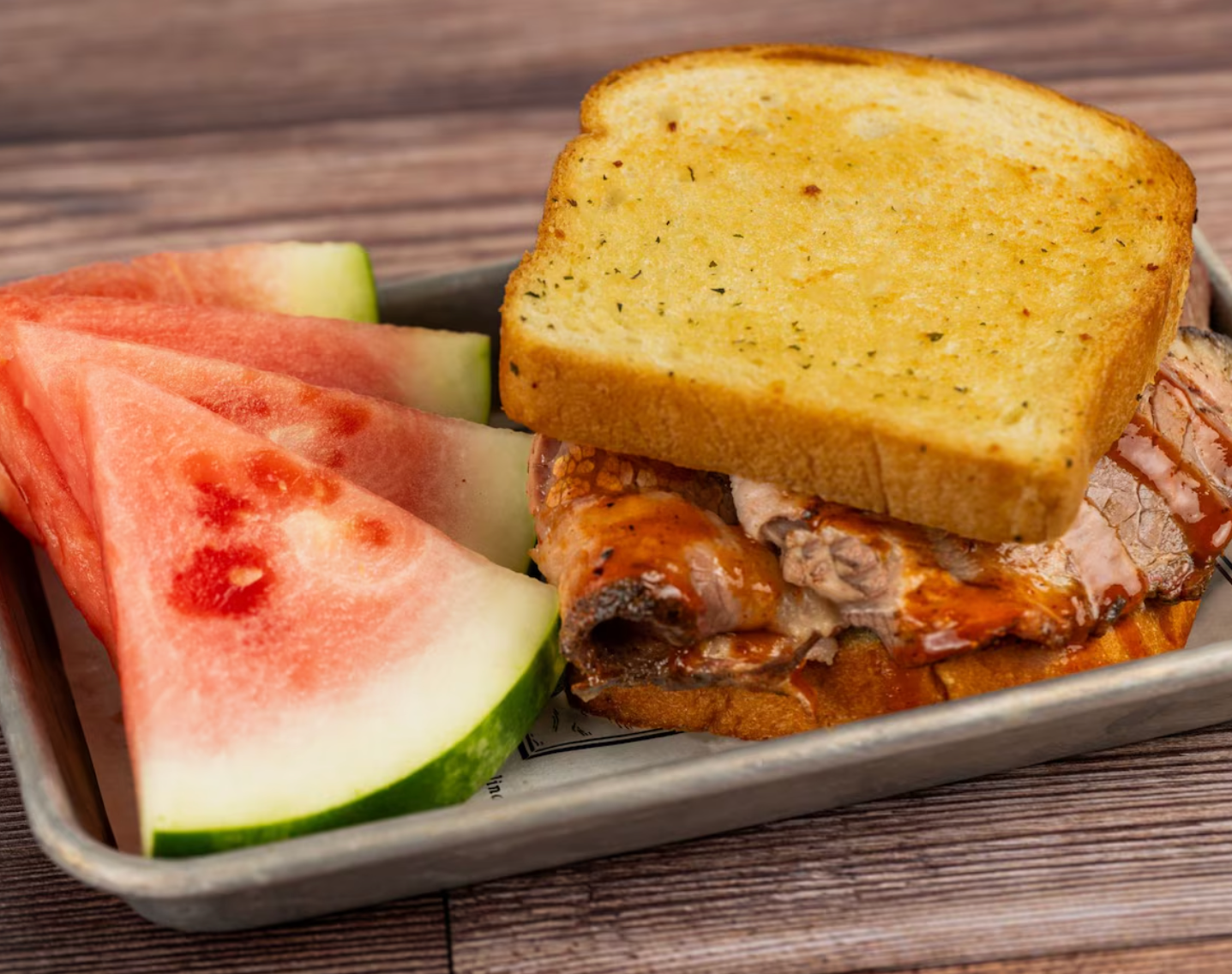 Grilled sandwich with pulled meat and watermelon slice on white plate.