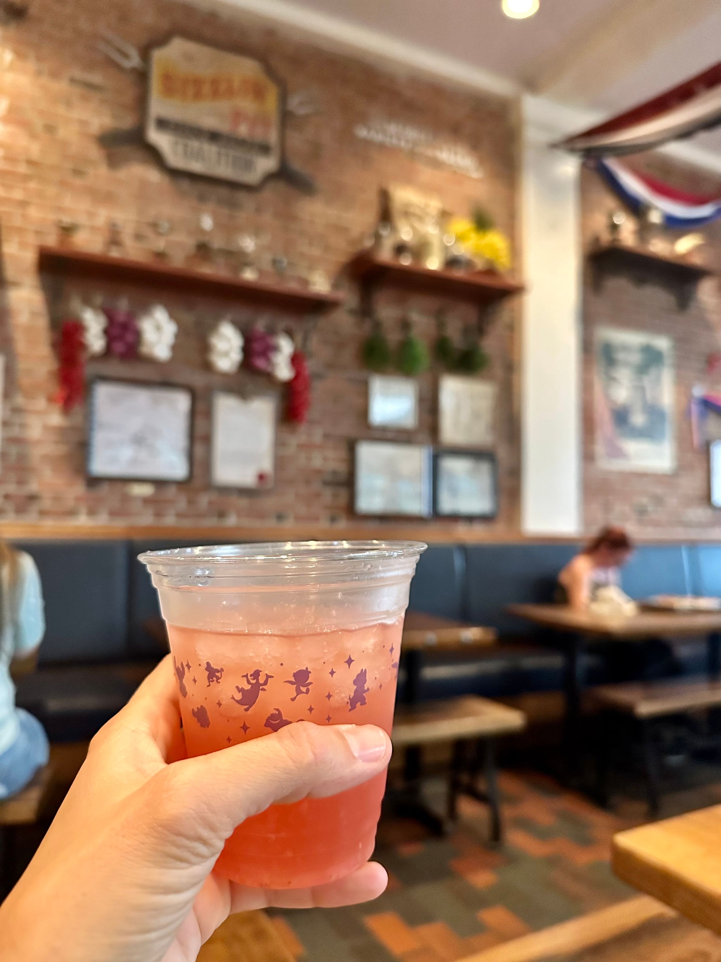 Pink beverage in clear plastic cup held against rustic restaurant interior.