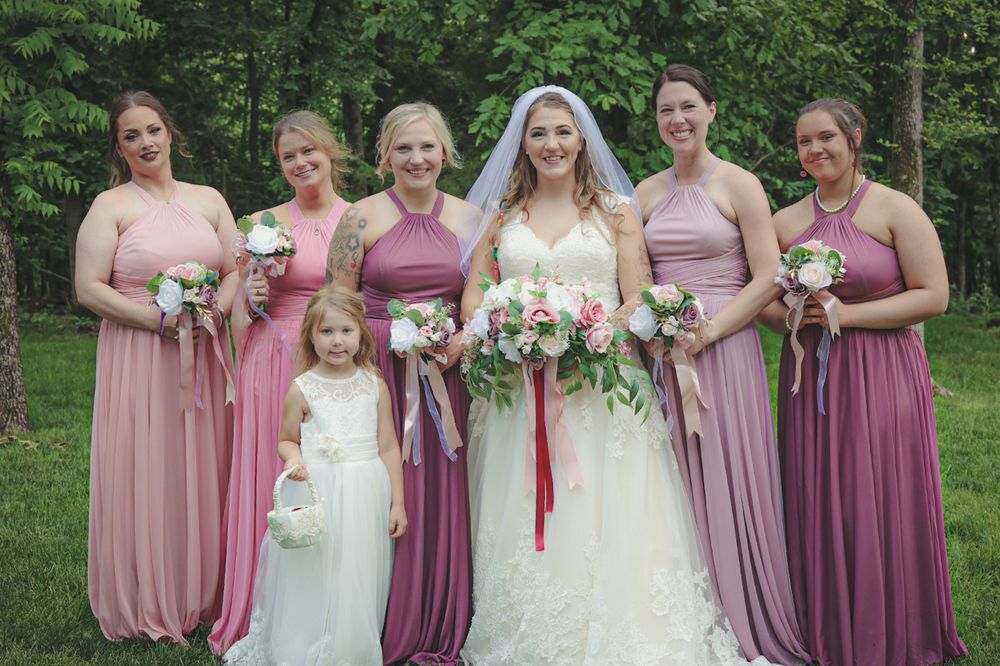 Wedding party in mauve and pink bridesmaid dresses poses together outdoors in a garden setting.
