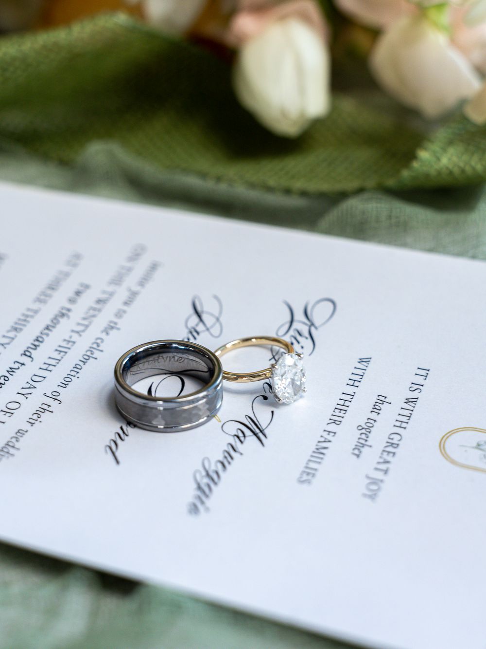 Wedding rings and invitation details artistically arranged on white paper with soft lighting.