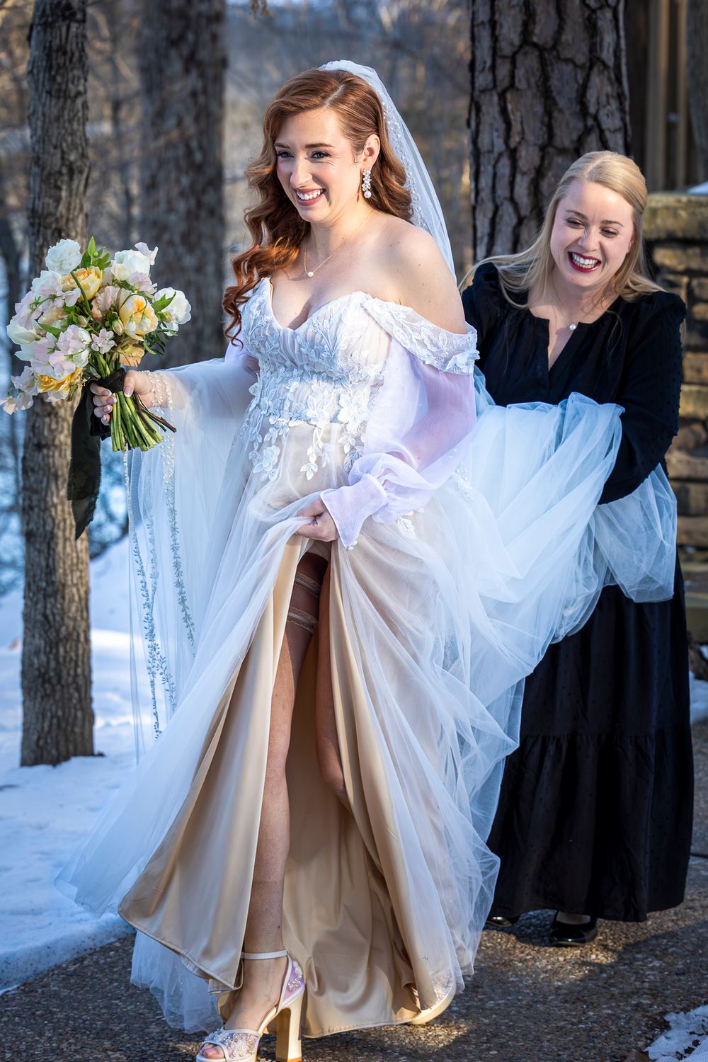 A bride in a white wedding dress lifts her skirt to reveal gold boots while standing in a snowy winter setting.