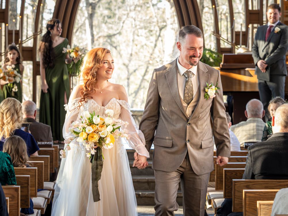 Joyful wedding couple and wedding party celebrate in a rustic wooden church with sunlight streaming through windows.