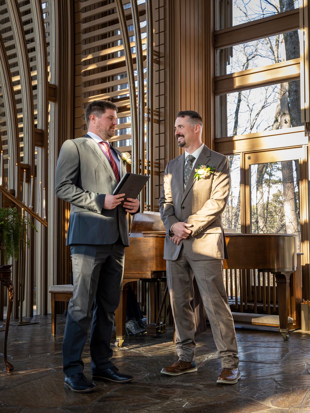 Groomsmen in suits playfully posing in a wood-paneled room with large windows.