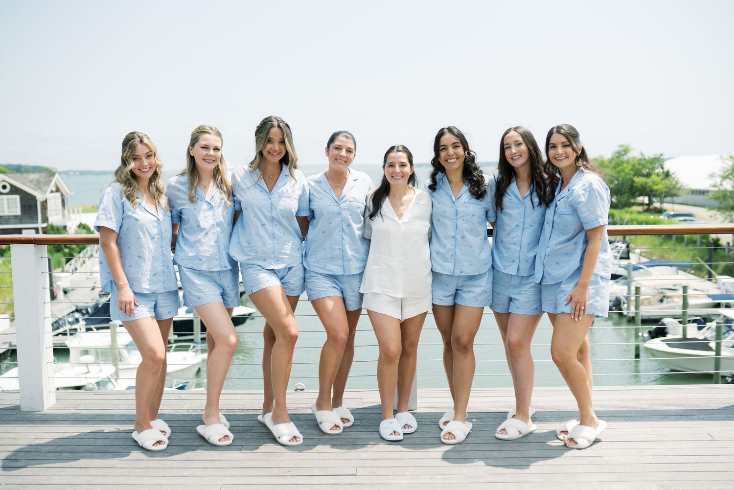 Wedding party members lined up wearing matching blue outfits on a waterfront deck.