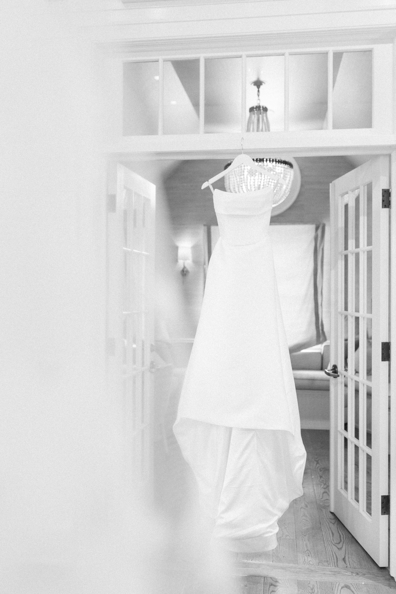 A white wedding dress hanging in a doorway with built-in shelving and natural light.