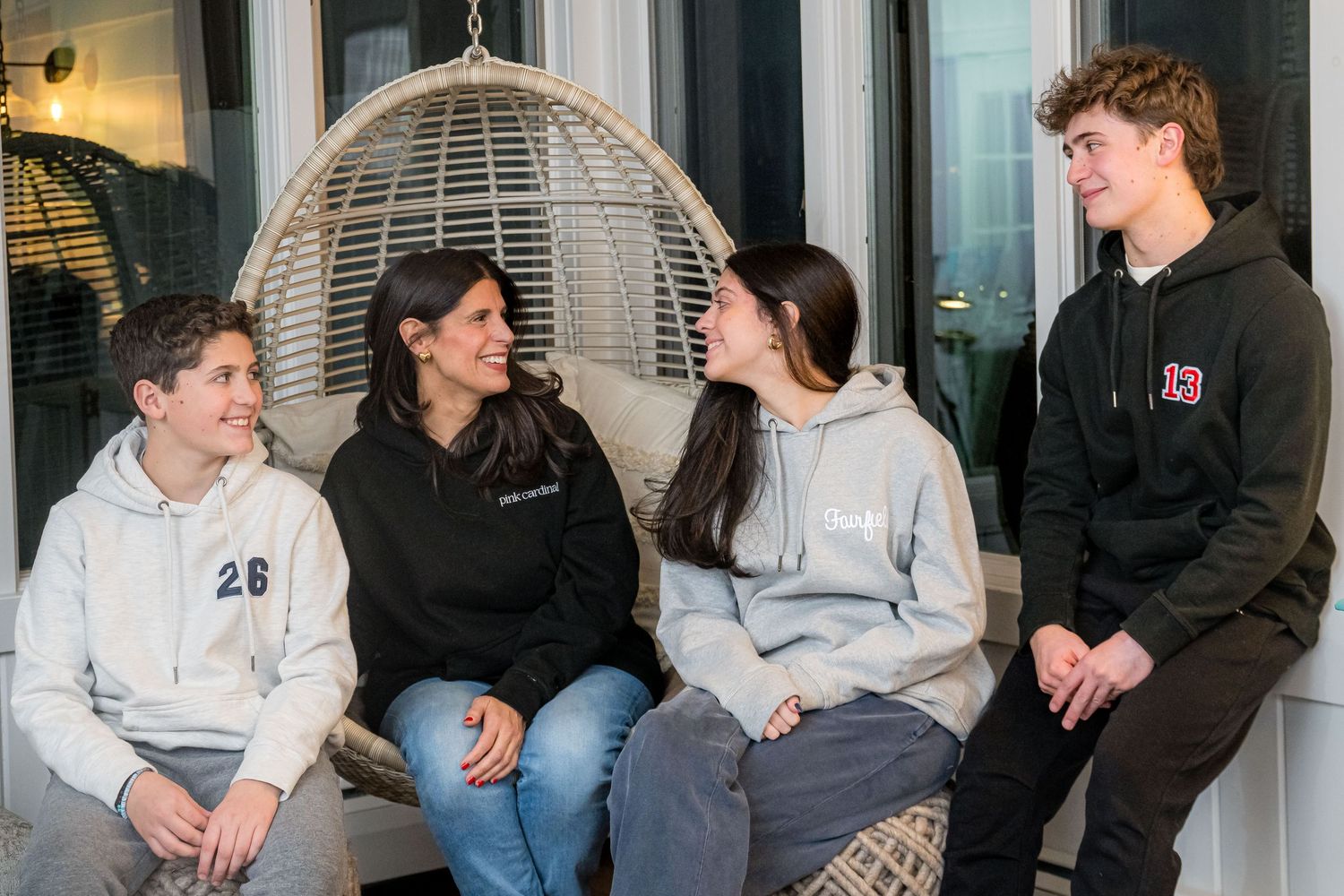 Group of students sitting and chatting together on a comfortable porch swing with a hanging egg chair in background.