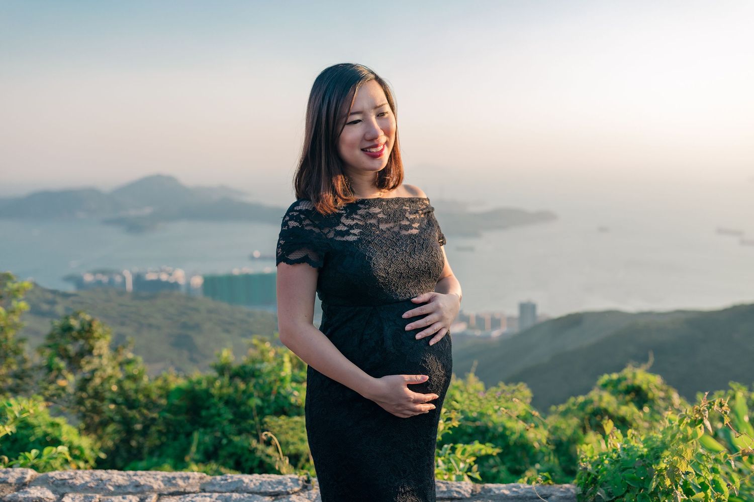 A maternity photoshoot with scenic mountain views taken at sunset showing someone cradling their baby bump.