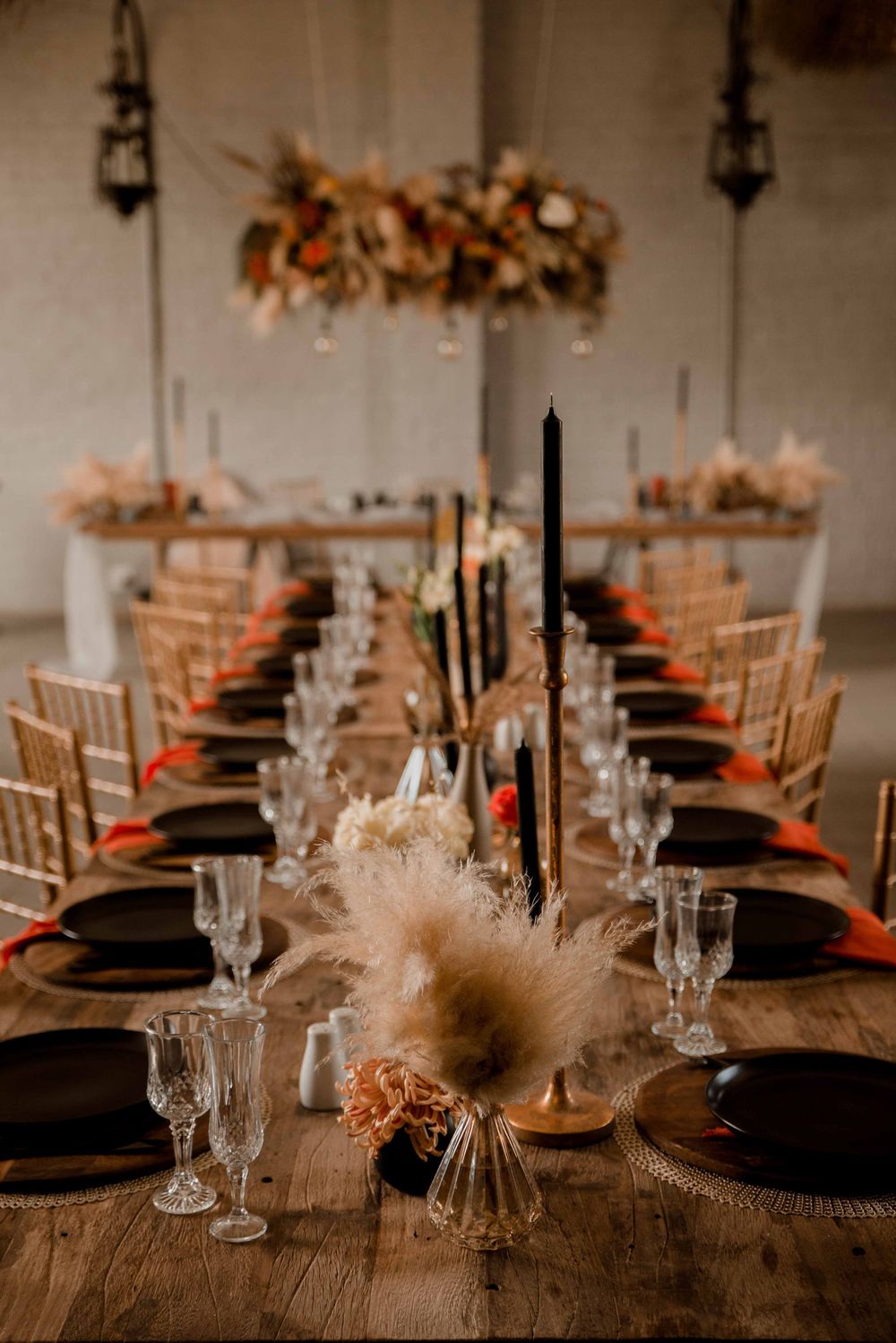 Bohemian fall wedding décor with rust orange and black accents, pampas grass, dried floral centerpieces, and warm candlelight