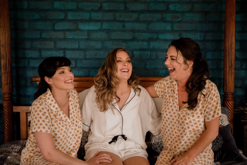 The bride and bridesmaids in their matching wedding pajamas laughing on the big four poster bed