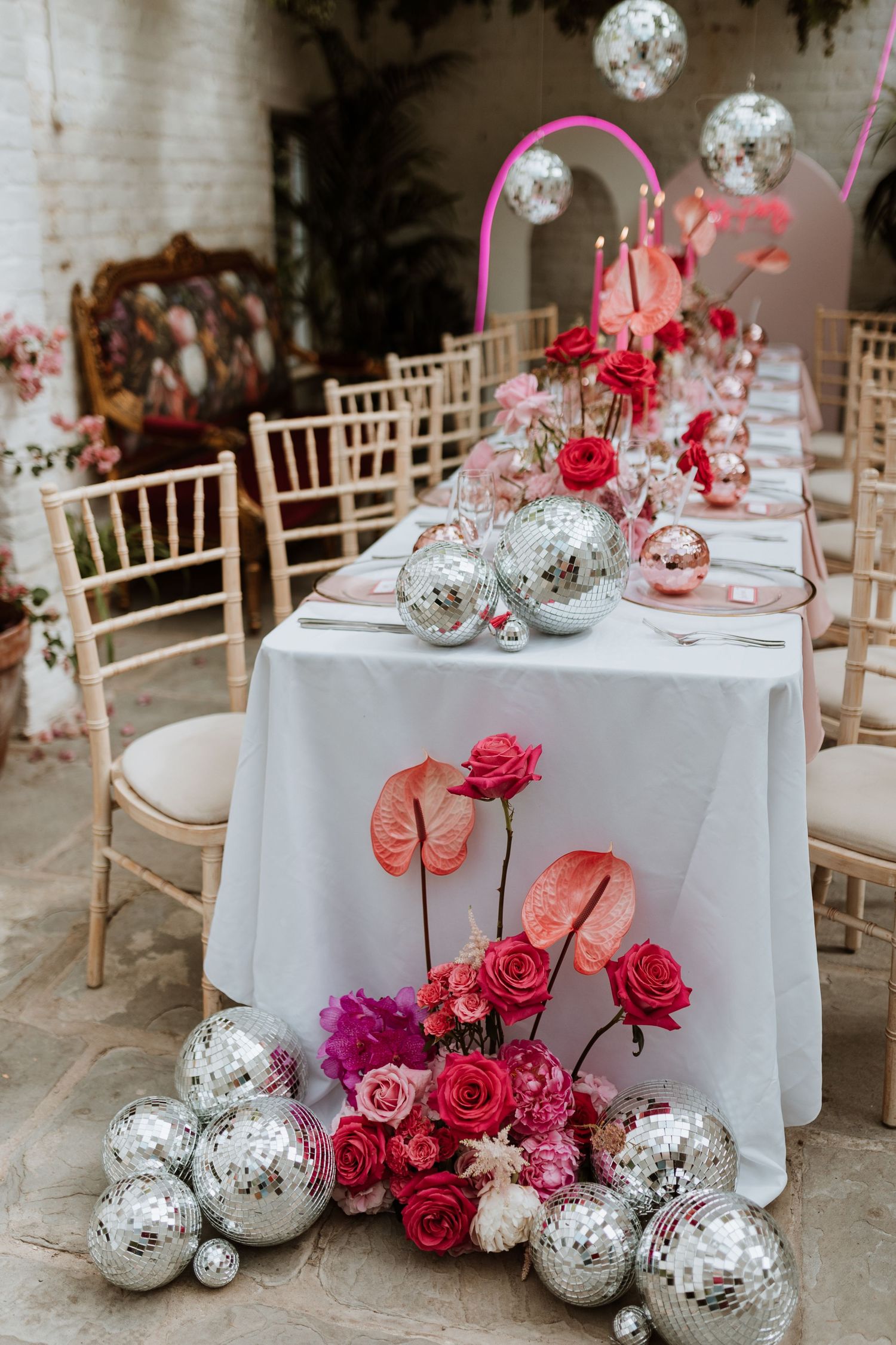 Wedding reception table decor features silver disco balls and vibrant pink roses for a modern glam celebration setup.