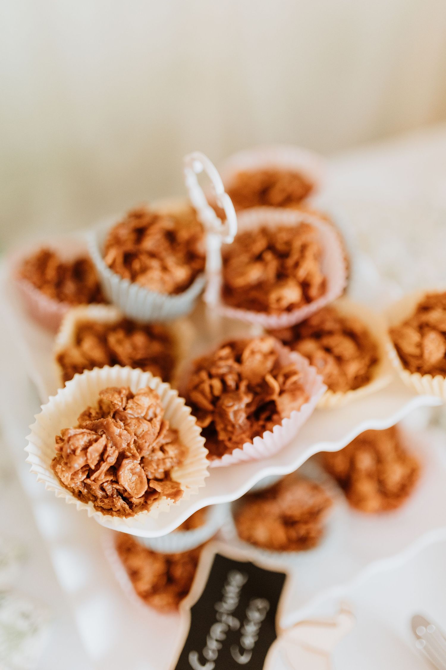 Homemade chocolate cornflake clusters arranged on a white tiered serving plate with rustic styling.