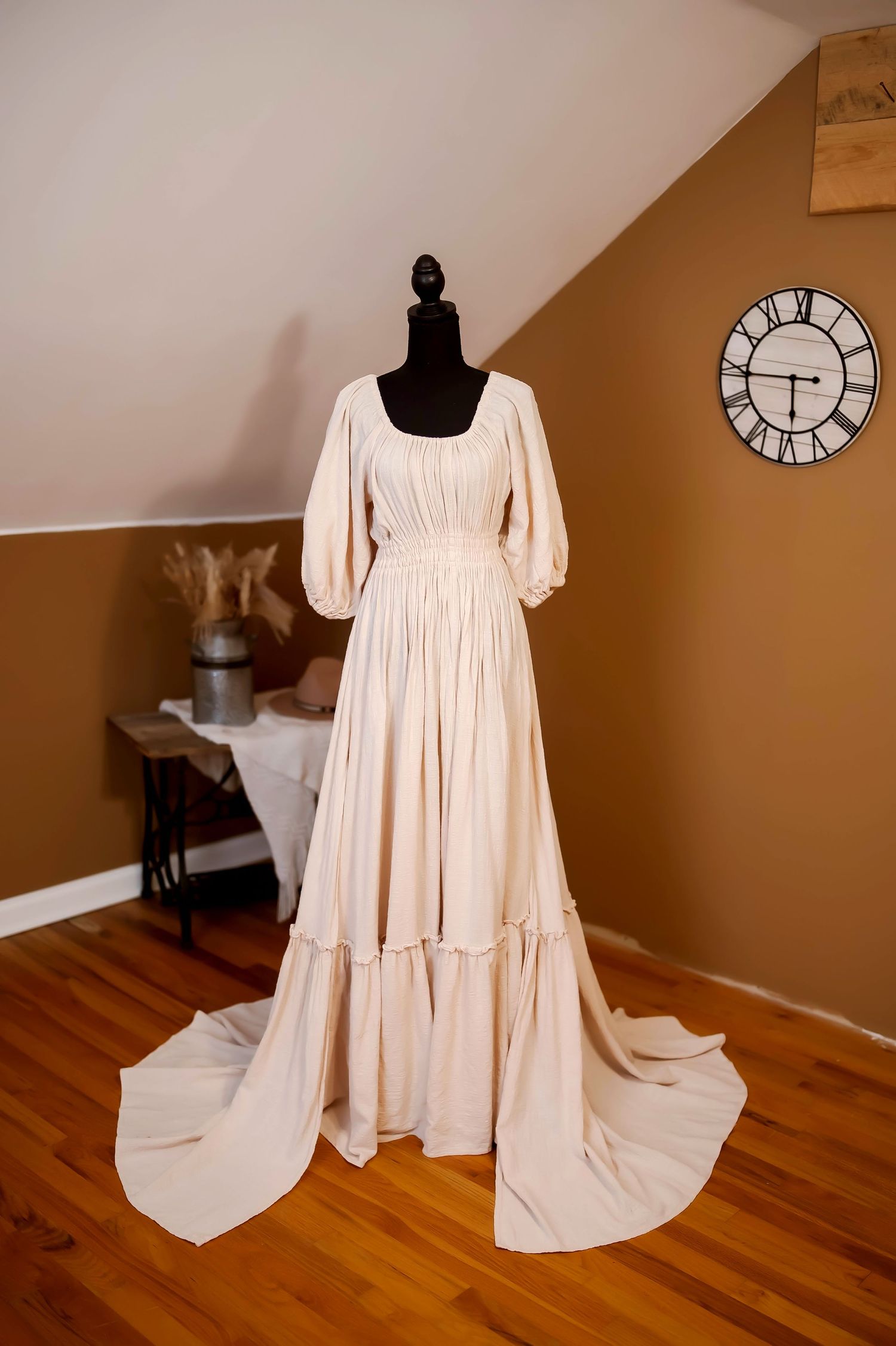 A flowy floral maxi dress displayed on a black mannequin with rustic room decor including a wall clock and wooden floors.