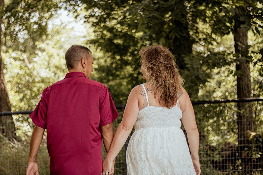 A couple in summer attire walking down a sun-dappled garden path together among lush greenery.