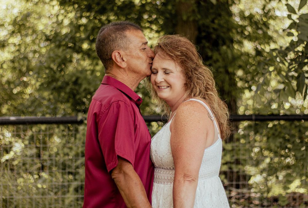 A tender romantic moment between a couple outdoors in a natural setting with greenery in the background.