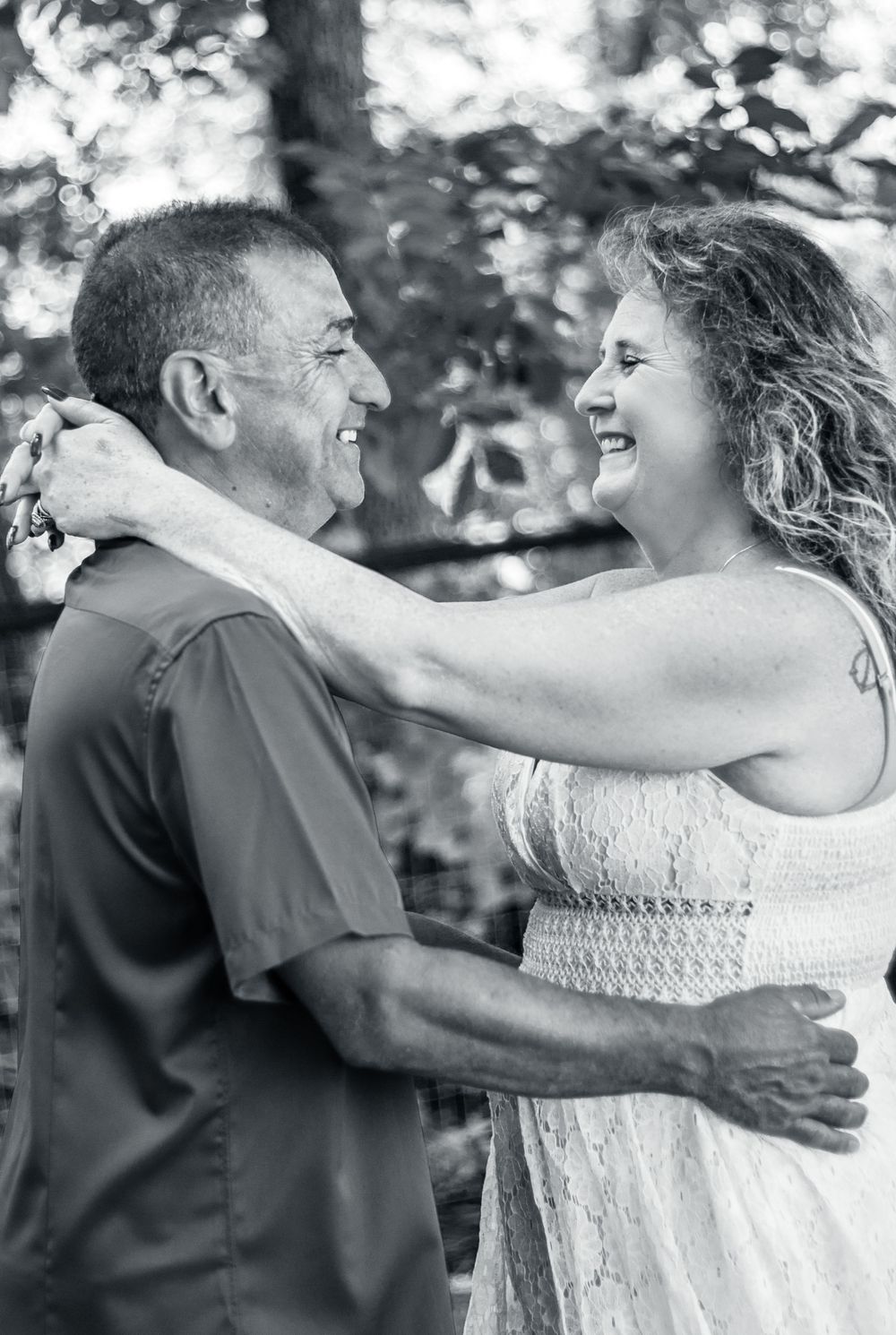 A sweet candid black and white portrait of a romantic moment between two people sharing joyful laughter outdoors.