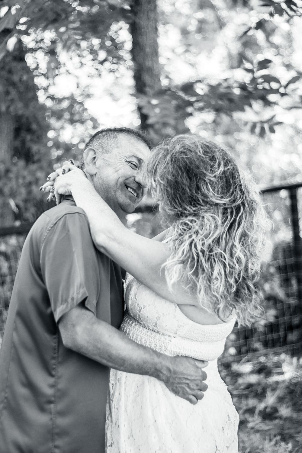 A joyful black and white photo of a romantic couple embracing and laughing together outdoors in a natural setting.