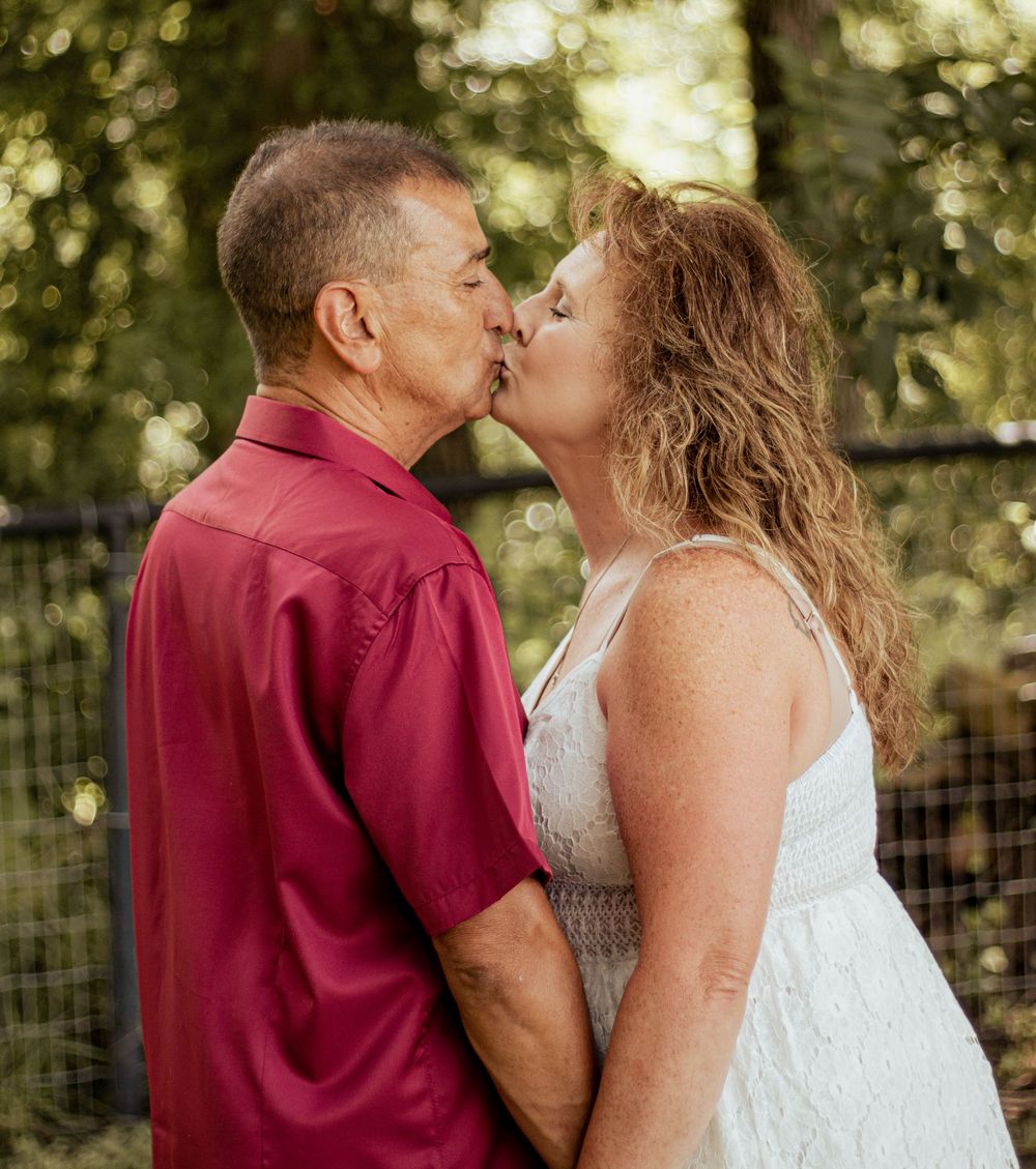 A couple shares multiple romantic kisses outdoors against a sunlit natural backdrop with trees and greenery.