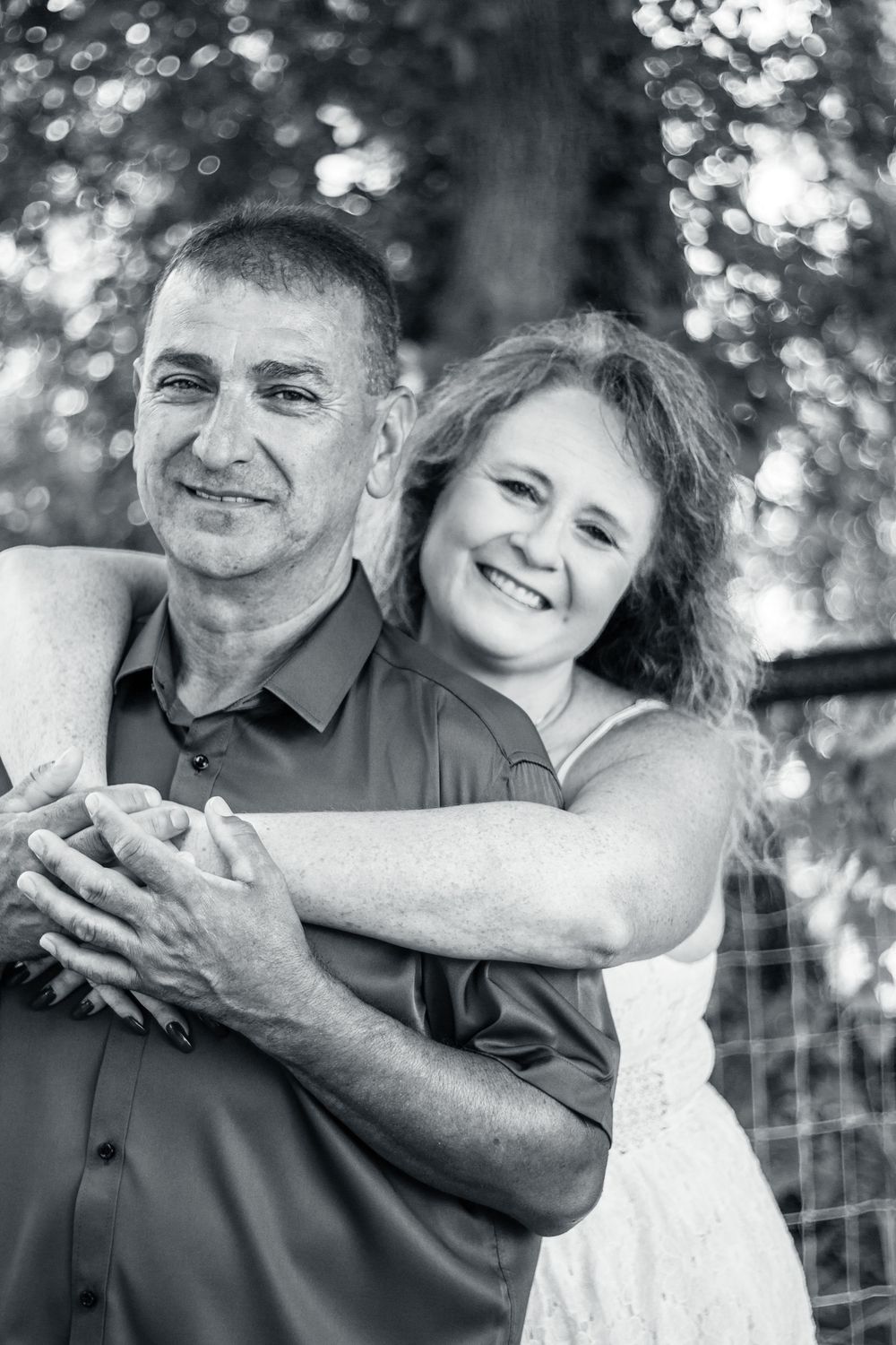 Black and white portrait of a happy couple embracing outdoors with soft bokeh background in nature.