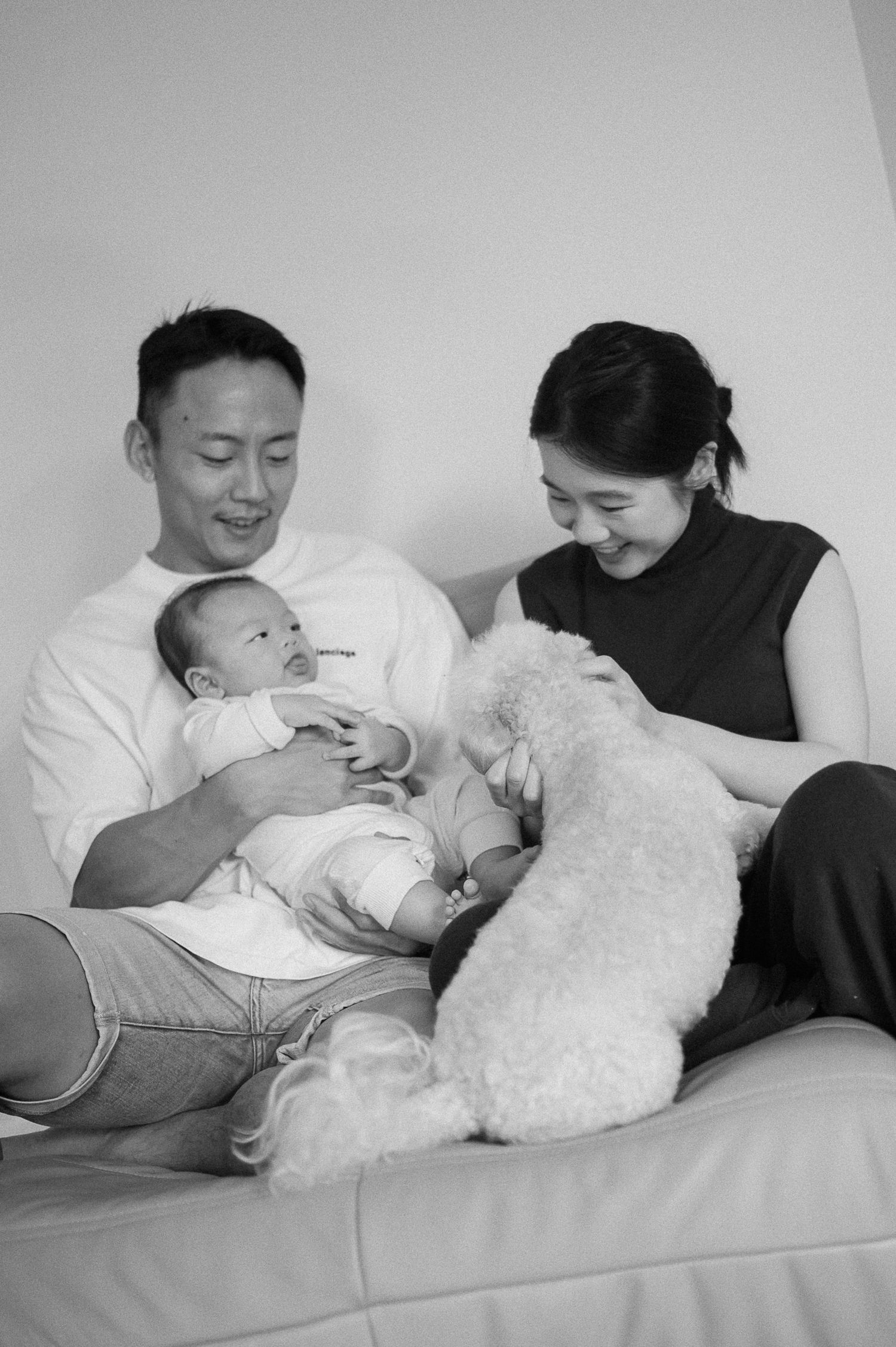 A family moment with a newborn and white cat on a cozy couch.