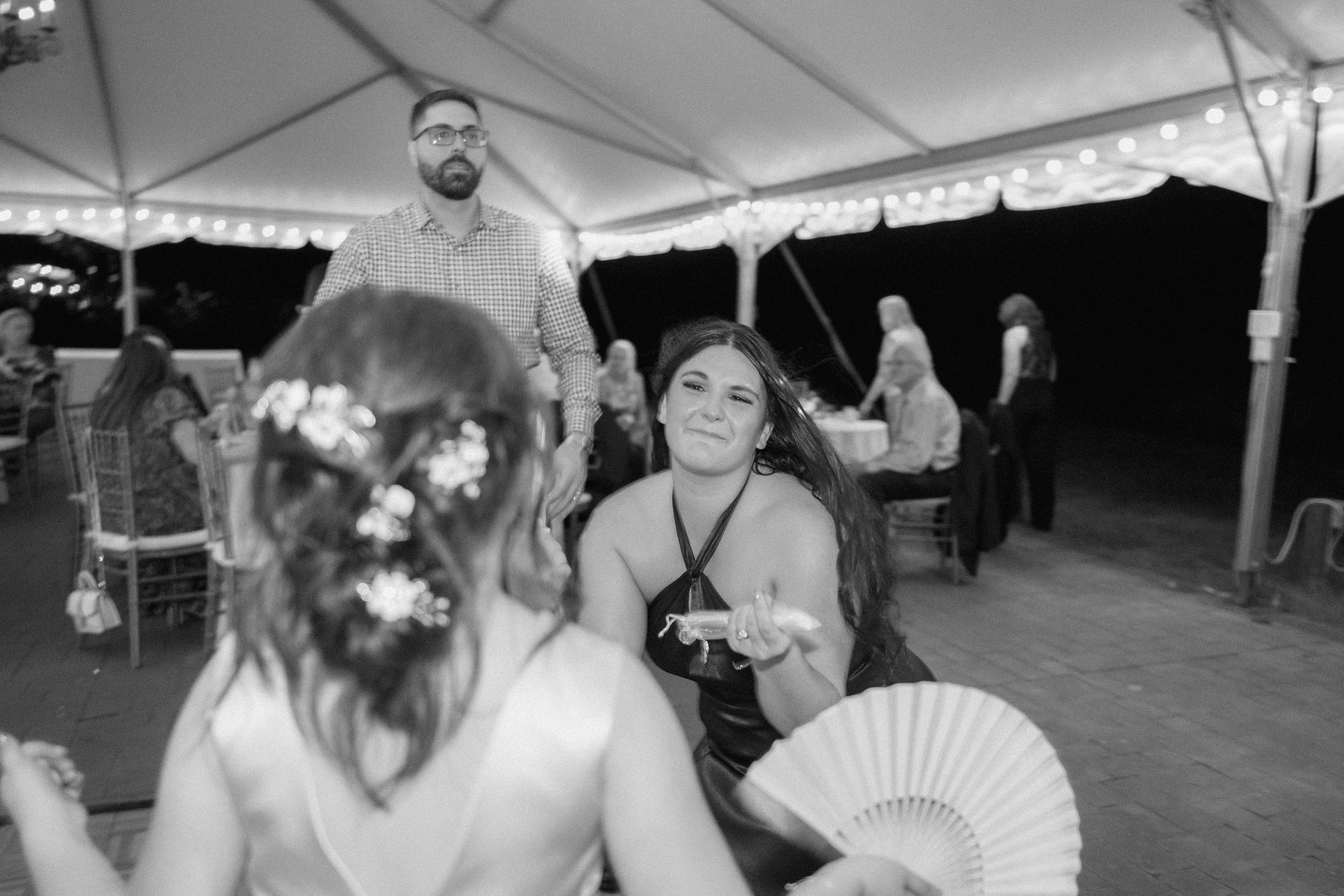 Guests dancing and celebrating with handheld fans under a white outdoor tent at an evening wedding reception.