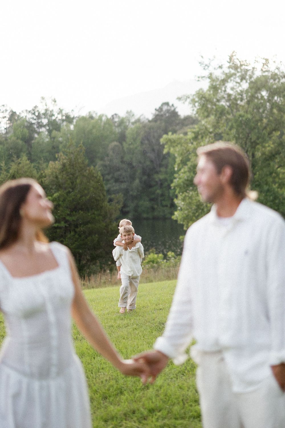 Three people in white outfits stand in a grassy field with trees in the background on a sunny day.