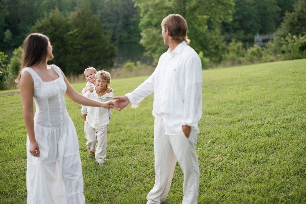 Family wearing all white outfits poses together in a grassy field during sunset photography session.