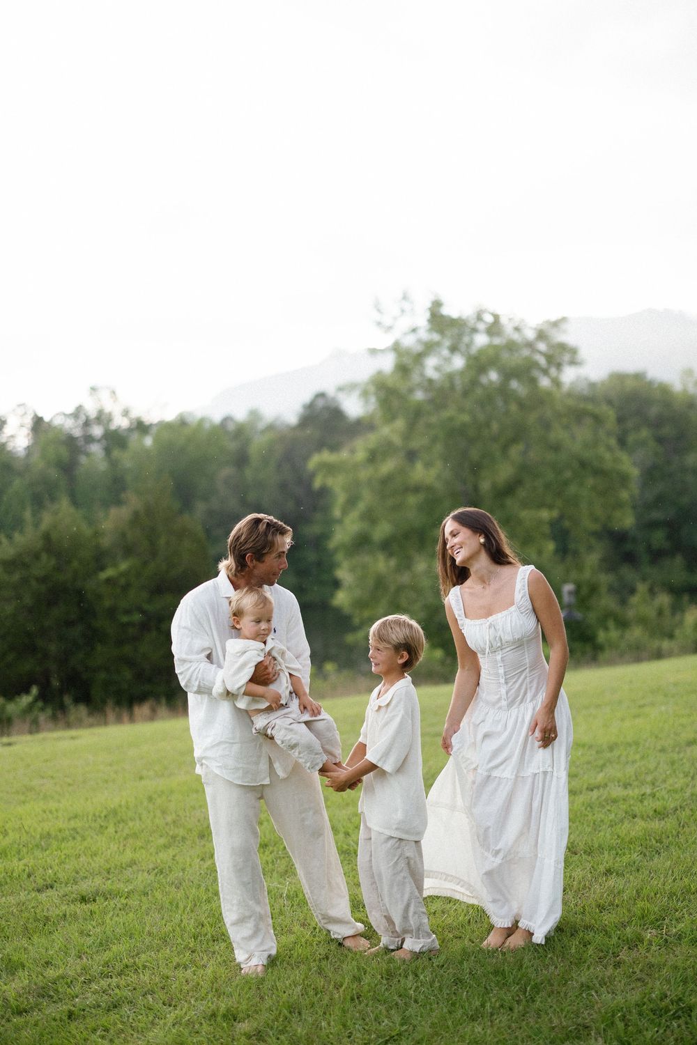 A family in white attire walking together on a grassy hillside during a summer day.