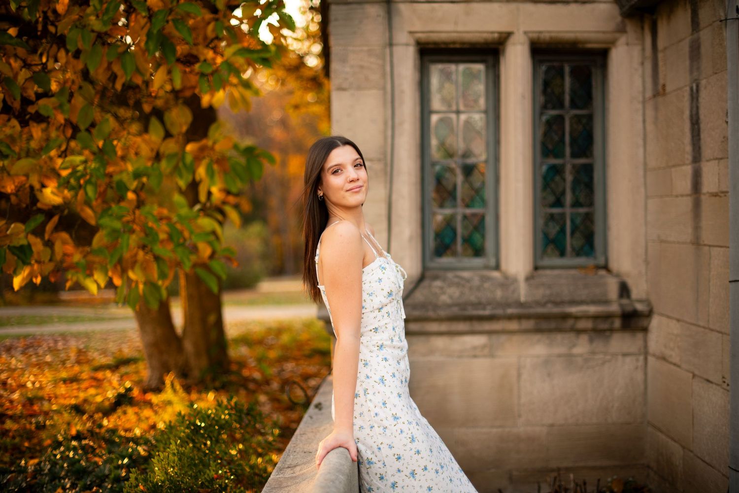 Bride in polka dot wedding gown poses against stone building with autumn foliage creating warm golden backdrop.