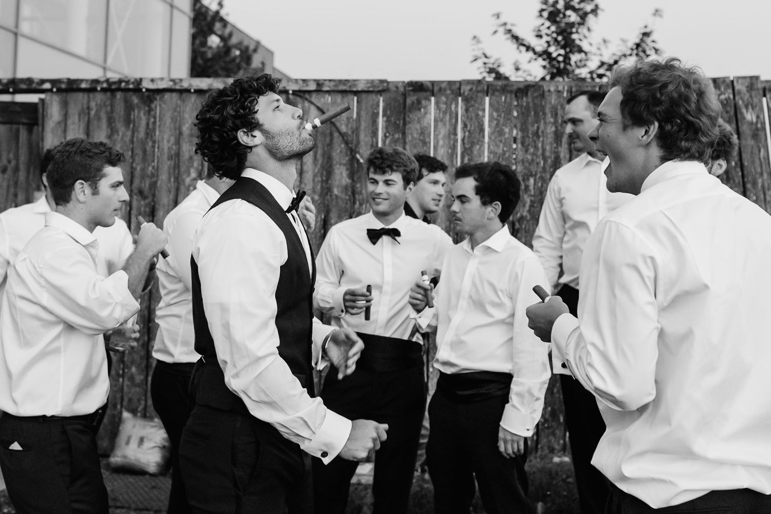 A group of young men in formal white shirts and suspenders gather outdoors socializing at a casual event.