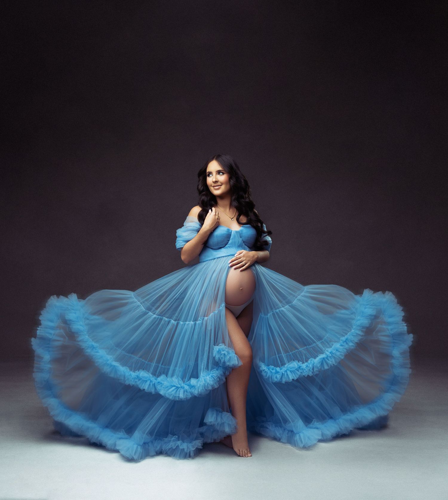 A dancer in a flowing light blue gown strikes an elegant pose against a dark backdrop.