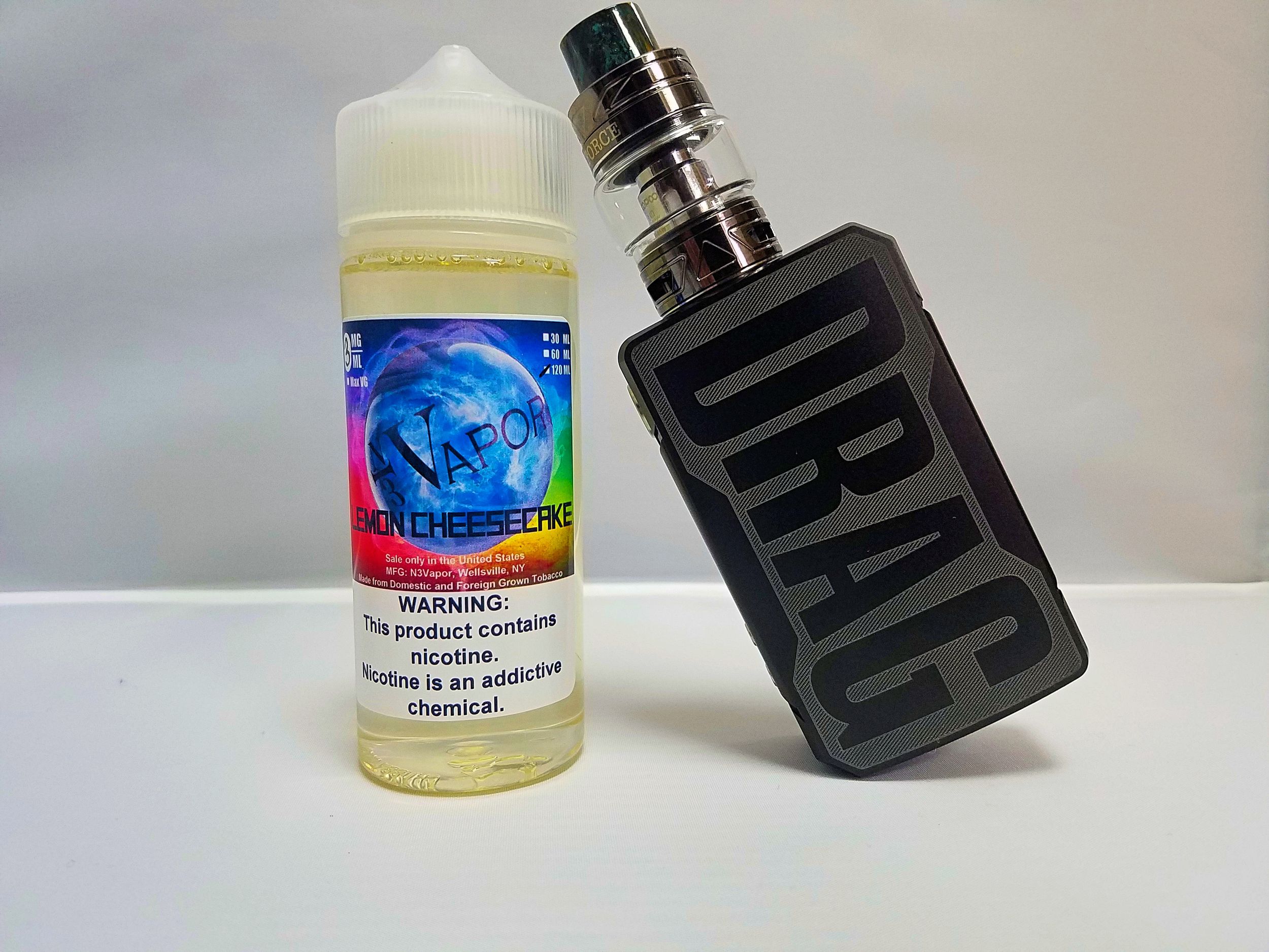 Black vape mod leaning against an e-liquid bottle with blue label.