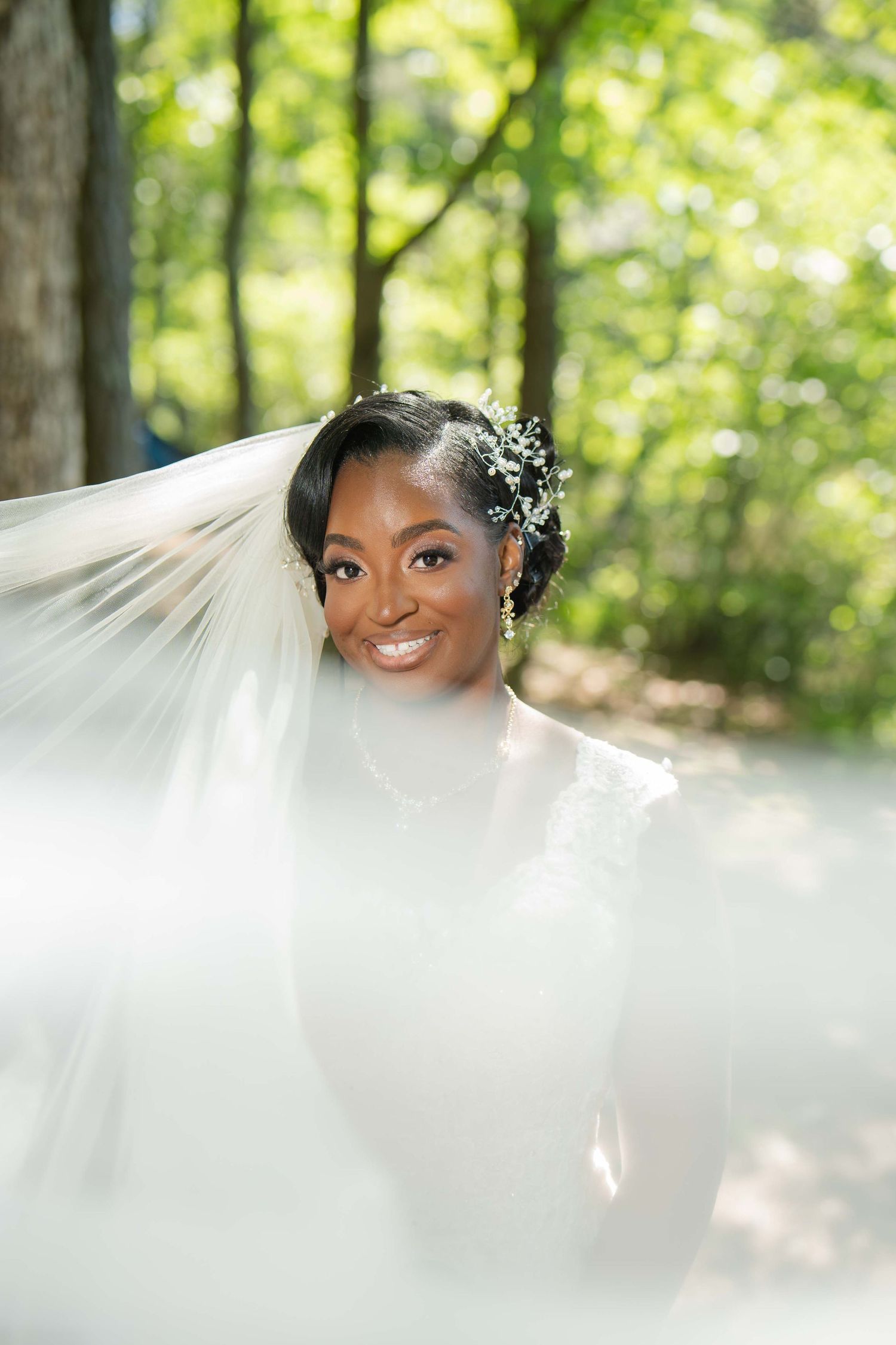 Wedding veil flowing in the breeze against a green forest background.
