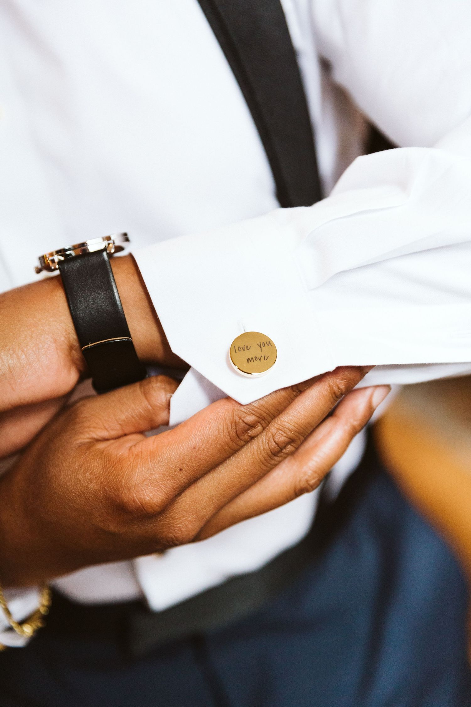 Close-up detail of cufflinks being fastened on a white dress shirt sleeve.