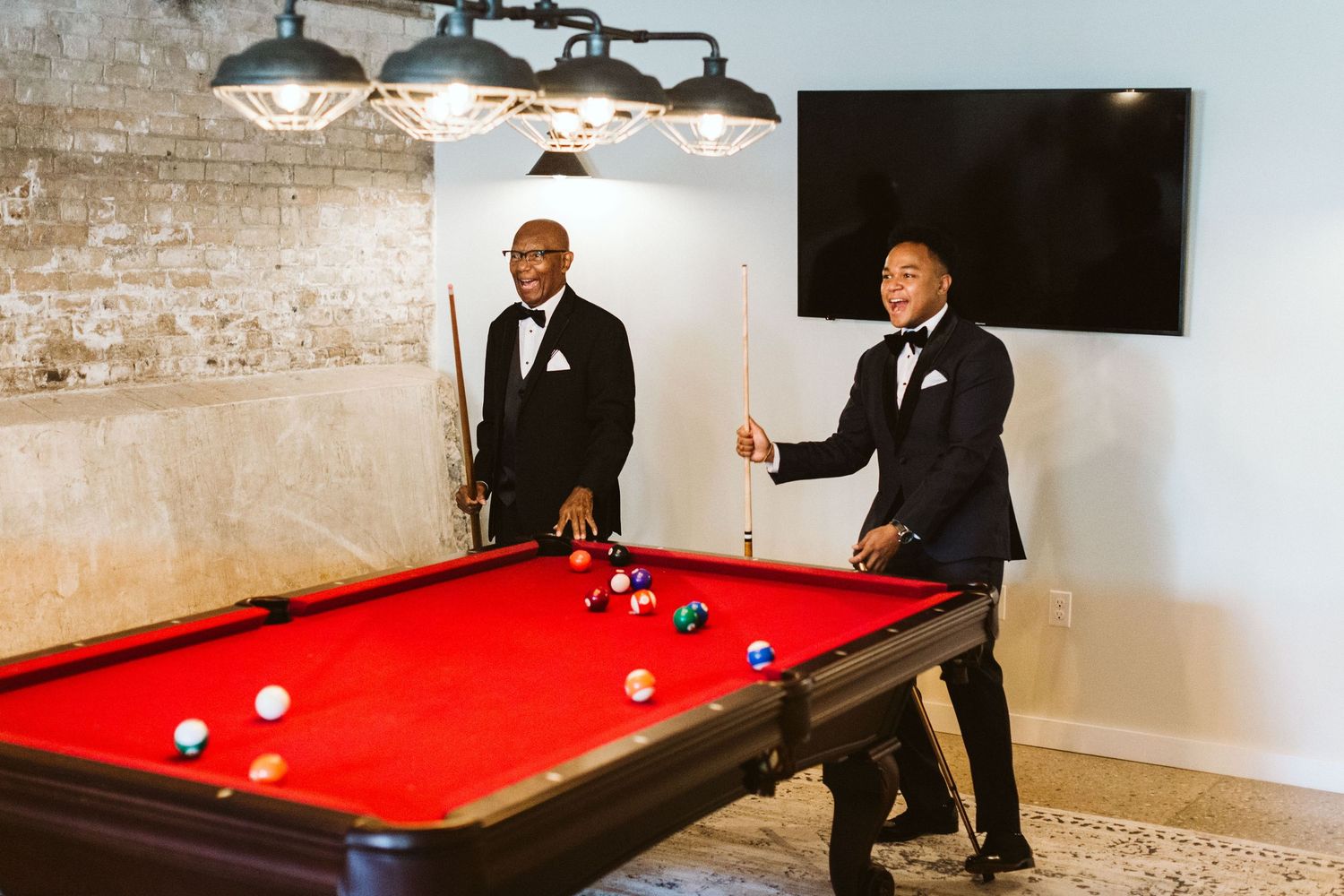 Friends playing pool on a red felt table in a brick-walled room.