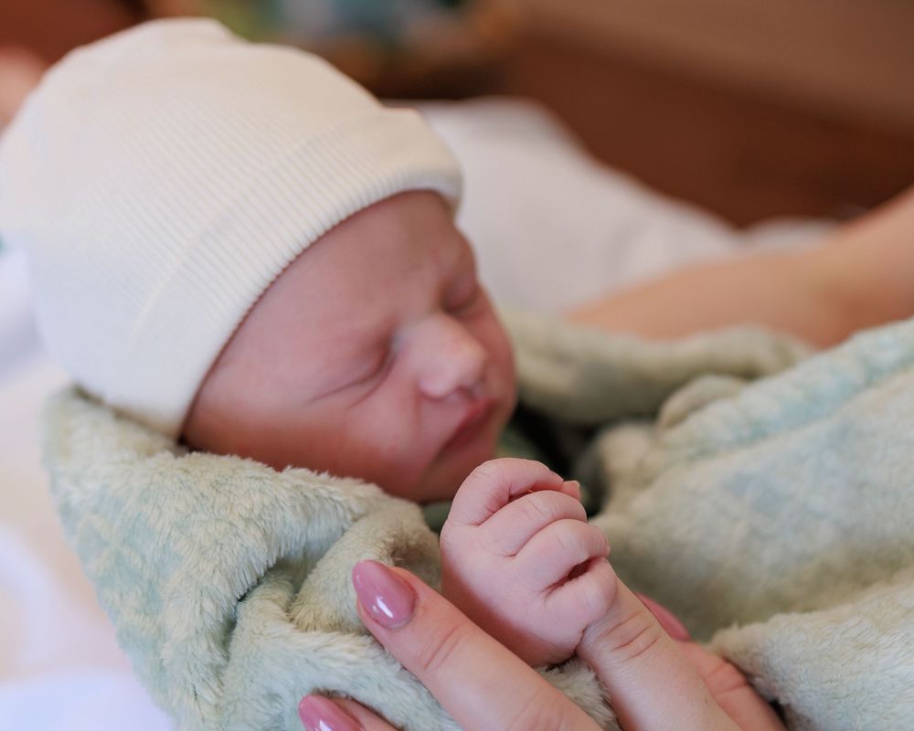 Peaceful newborn wearing white cap and swaddled in soft mint green blanket.