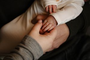 A small infant's hand reaches out to touch an adult's palm in an intimate black and white photograph.