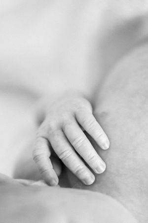 Black and white macro shot of a tiny infant hand resting on soft fabric.