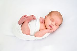 Artistic series of peaceful sleeping newborn photos in white swaddle against light background.