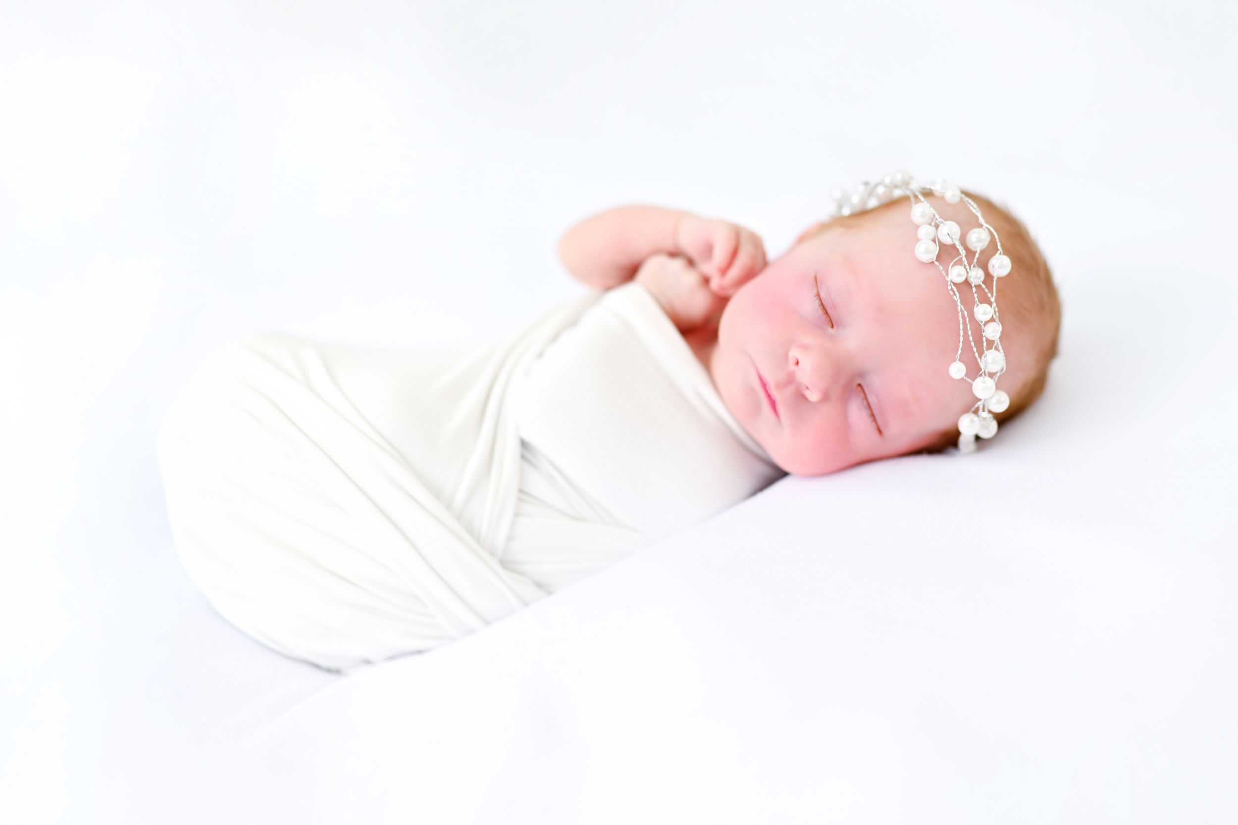 Artistic newborn photography with white backdrop and minimalist styling.